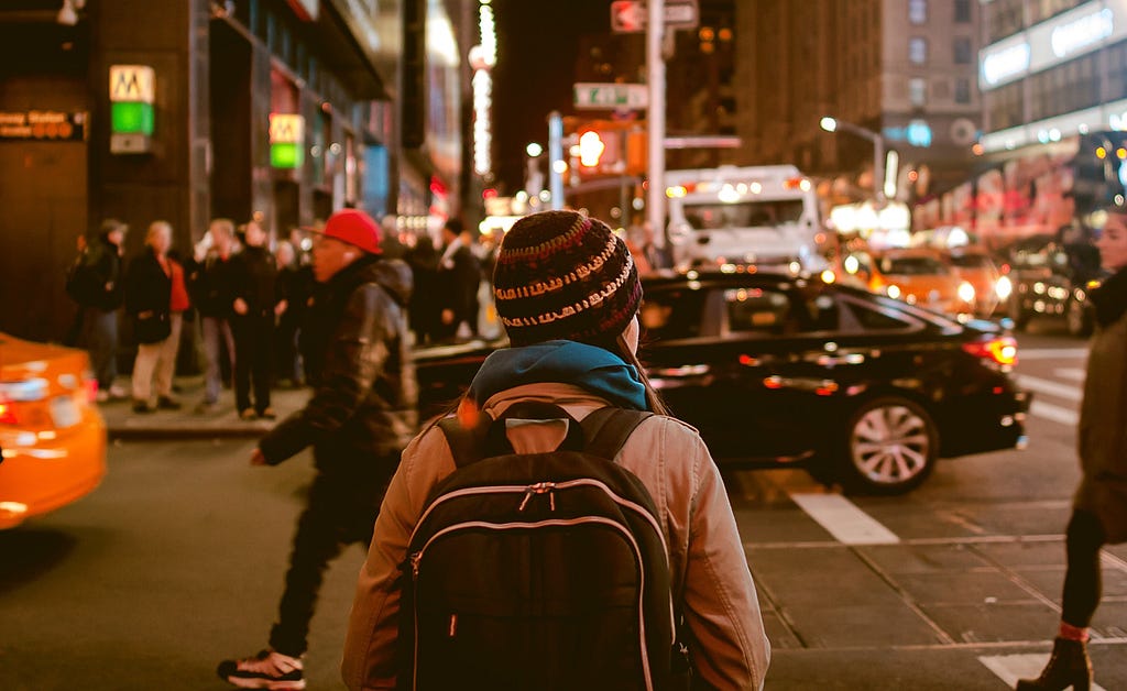 Person standing, facing a busy street of traffic and people.