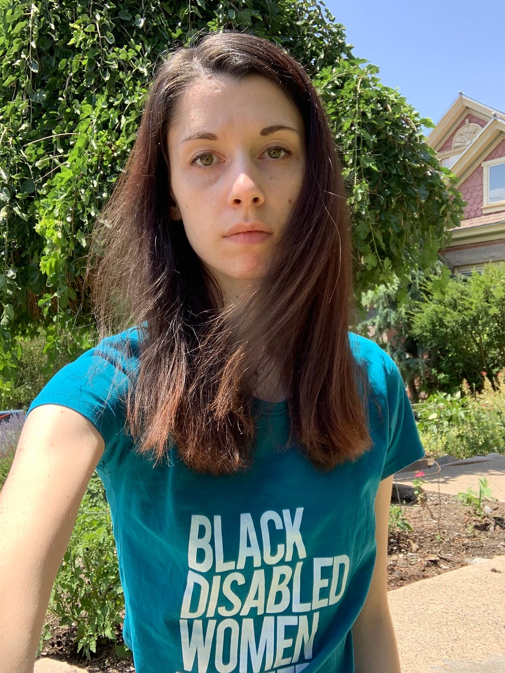 Selfie of Summer standing outside. Her face looks strong, and she wears a shirt that says “Black Disabled Women Matter.”