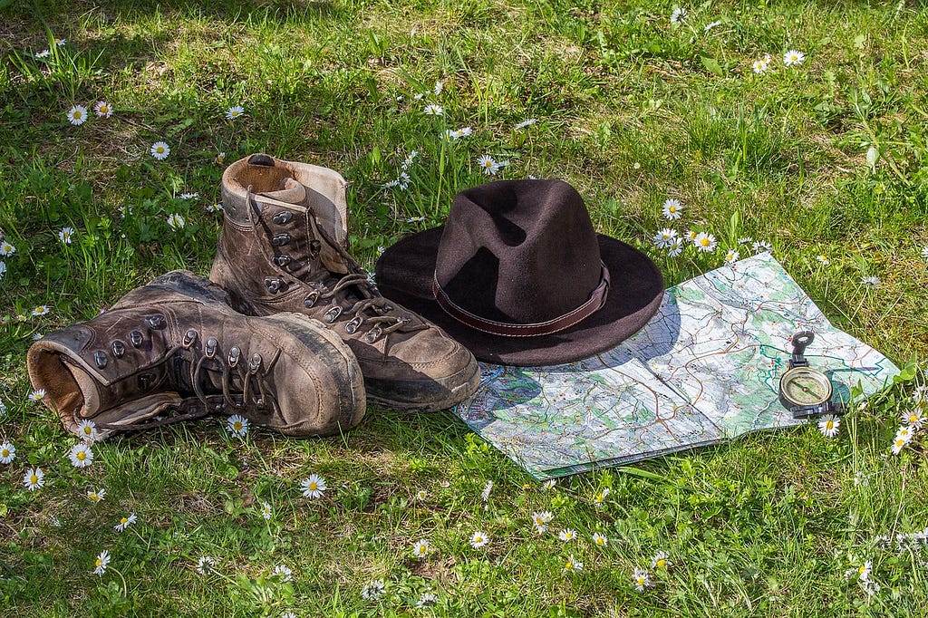 Hiking boots, hat, map, and compass on grass with flowering clover