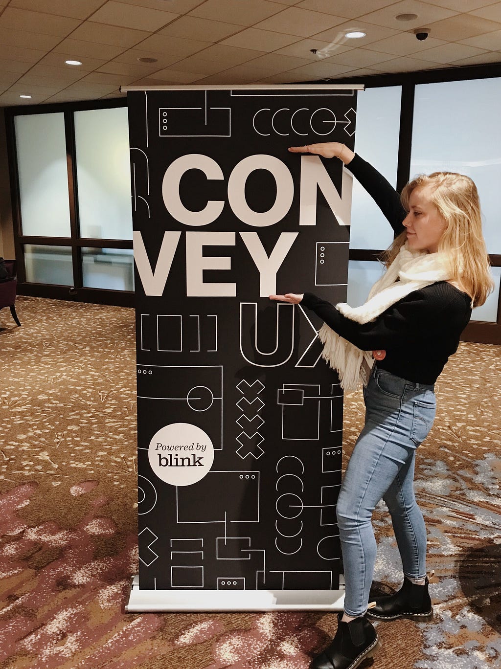 Julianne poses next to a tall poster that says “Convey UX, powered by Blink”