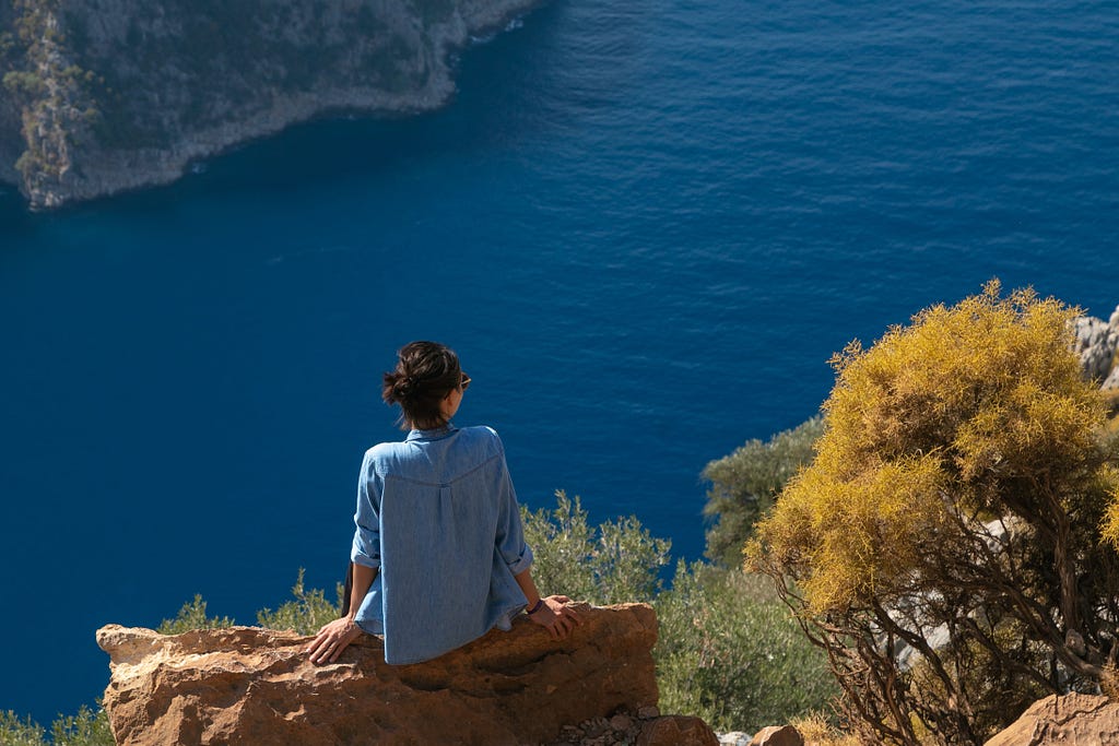 Woman sitting on a rock looking out over the ocean.