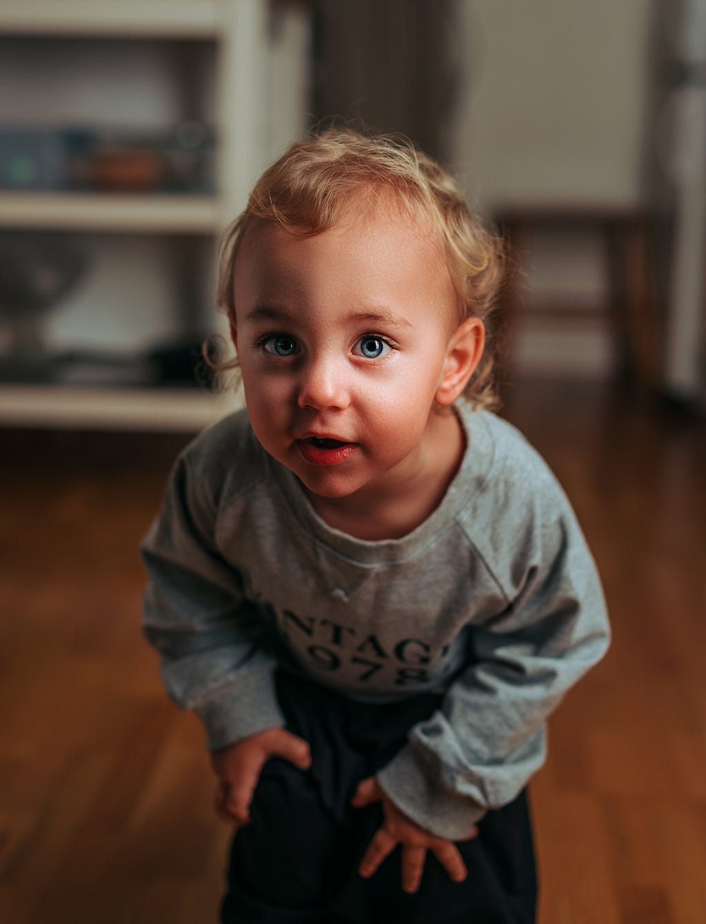This is a baby child. He is wearing a grey T-shirt. His eyes are light blue. His complexion is white. His hair is golden brown. This child appears to be highly sensitive.