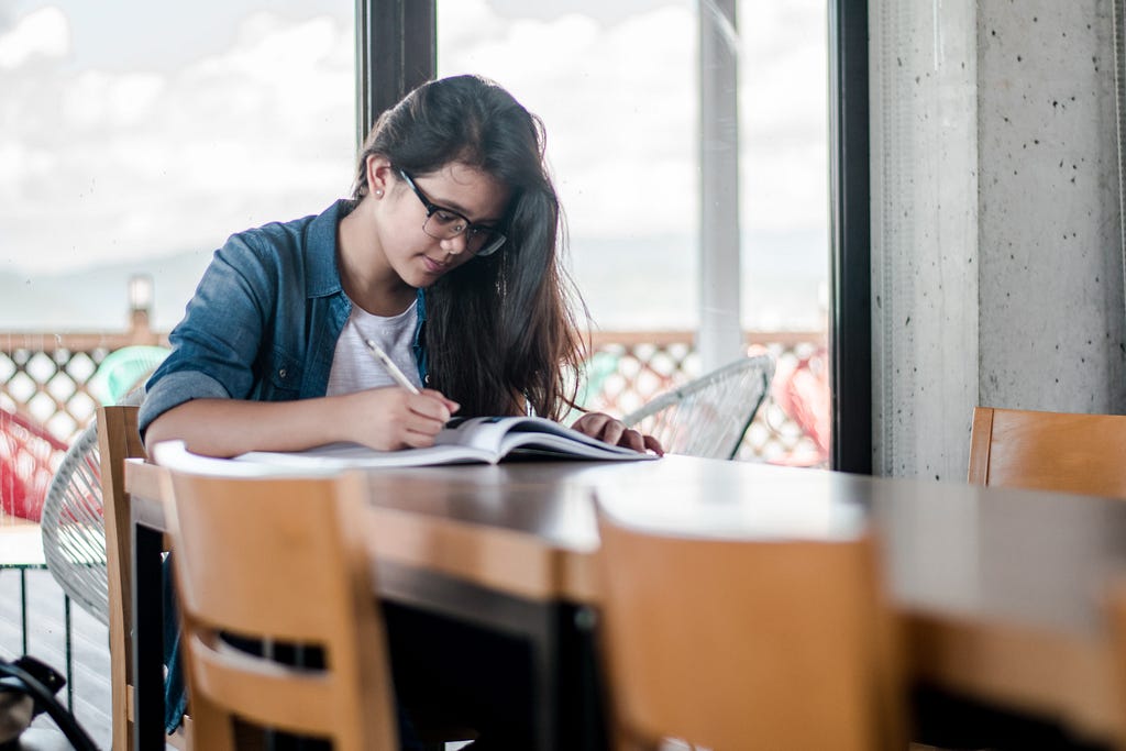 A white student sits at the end of a table reading a book