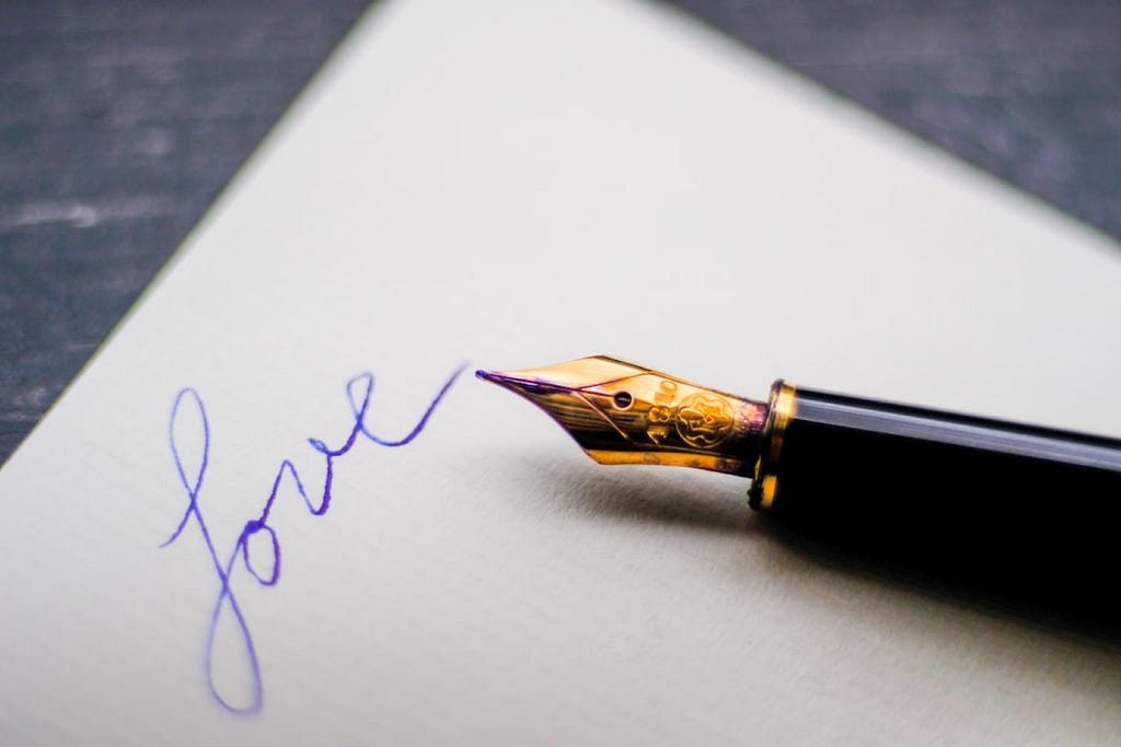 A fountain pen rests on paper with the word ‘Love’