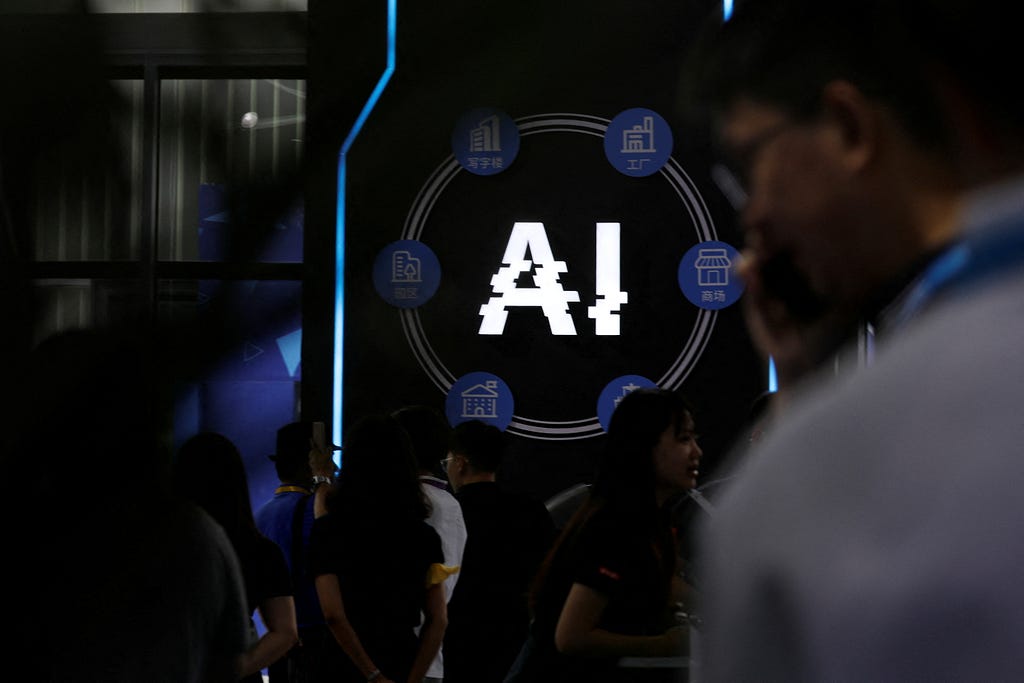 “AI” on a screen in a dark room with people milling around. Photo by Florence Lo/Reuters