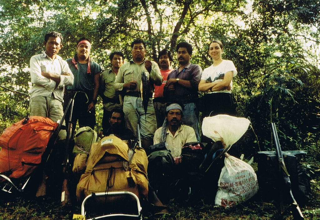 A group of people stand in front of their backpacks in a forest