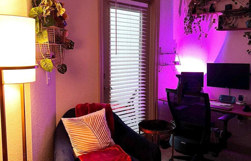 Image of a peaceful home office space including a comfy reading chair next to a floor lamp, and a desk with purple lighting.
