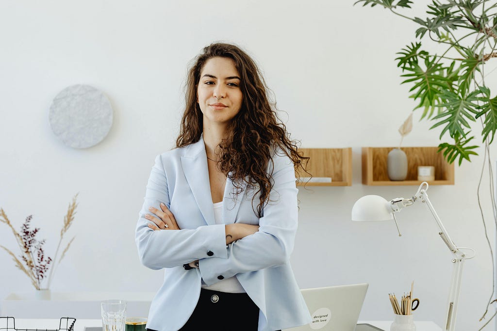 Woman in sky blue blazer standing next to white wall in office