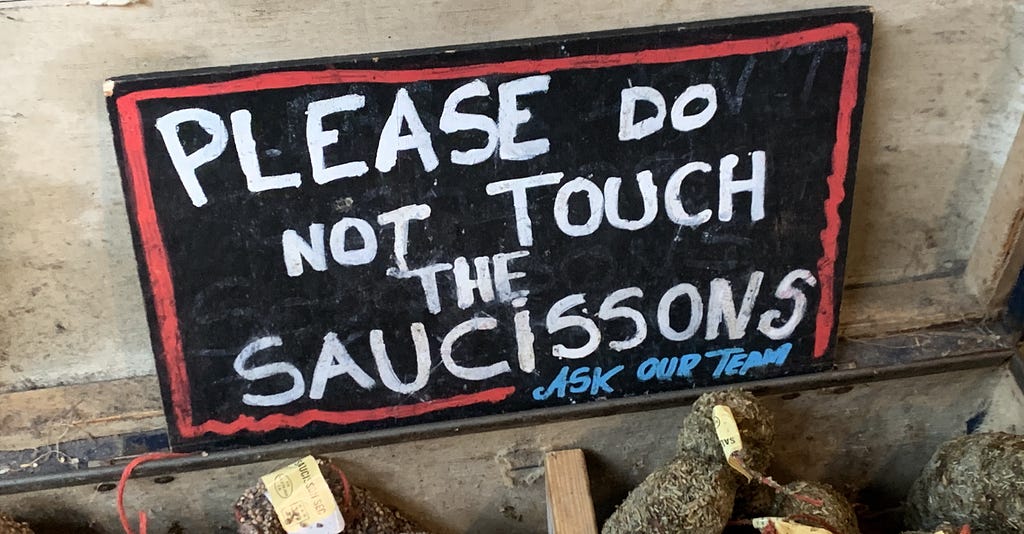 A market sign saying “Please do not touch the saucissons”