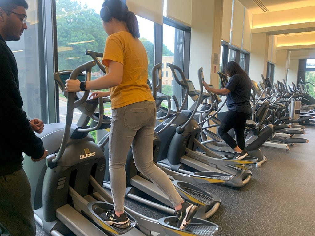 A student wearing yellow using the elliptical
