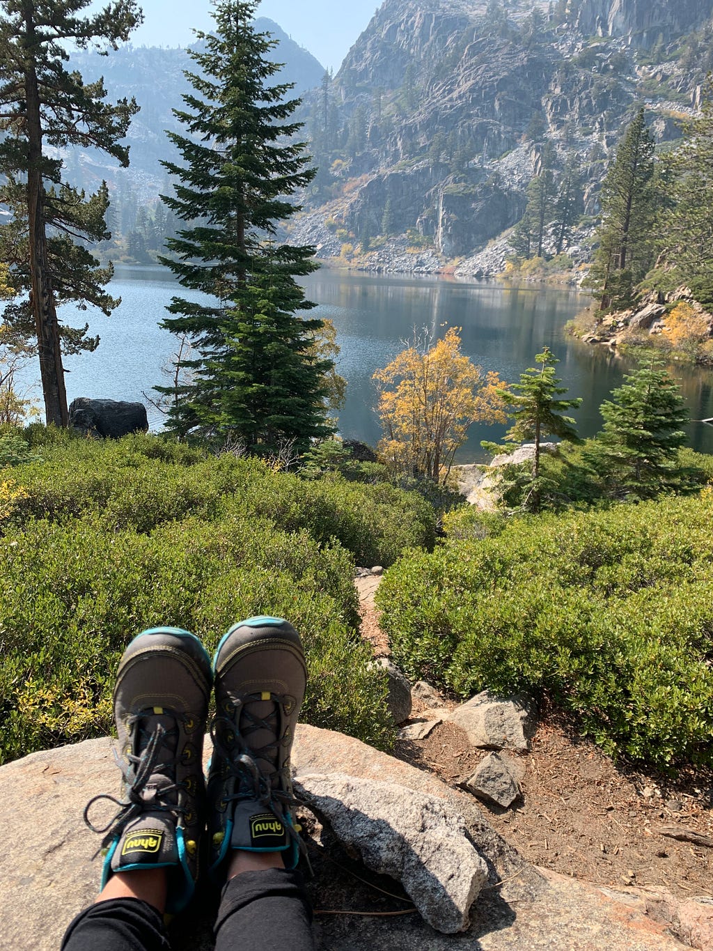 a beautiful lake surrounded by green trees with a pair of hiking boots in view