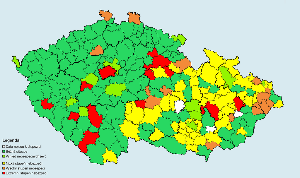 Mapa České republiky rozdělená na okresy, které jsou náhodně vybarvené zelenou, žlutou, oranžovou a červenou barvou.
