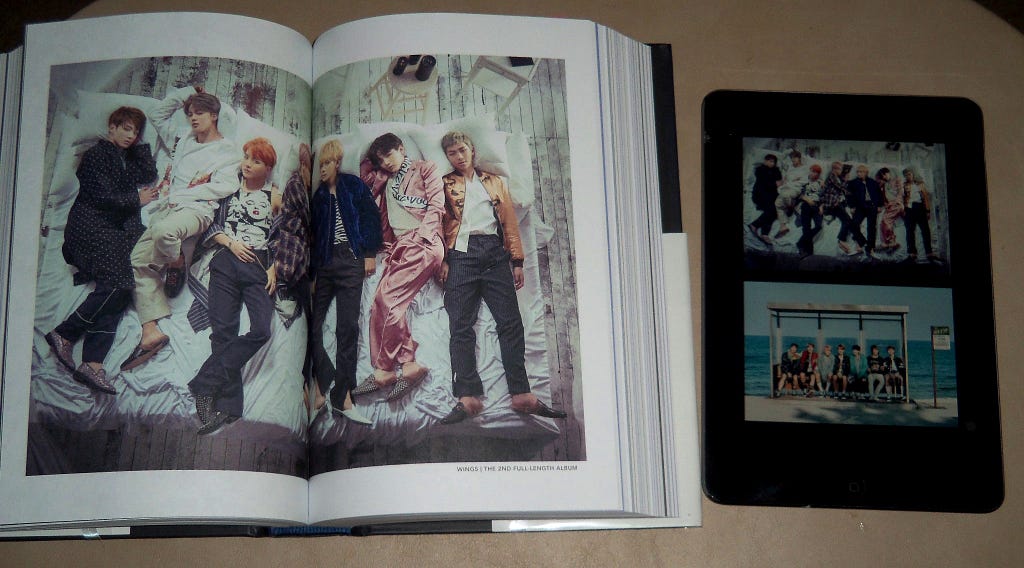 The BTS book open to a full-page spread of a picture next to the iPad with the same picture smaller and stacked on top of another picture.