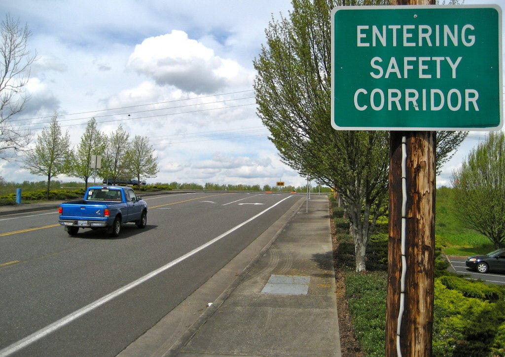 A truck drives past a green road sign that reads, “ENTERING SAFETY CORRIDOR”
