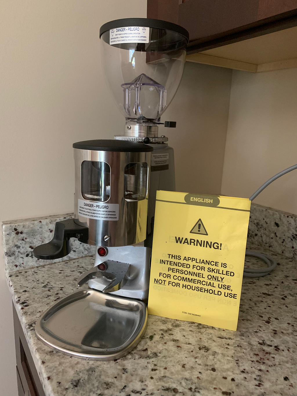 A coffee grinder with a yellow piece of paper next to it that says warning in large text.
