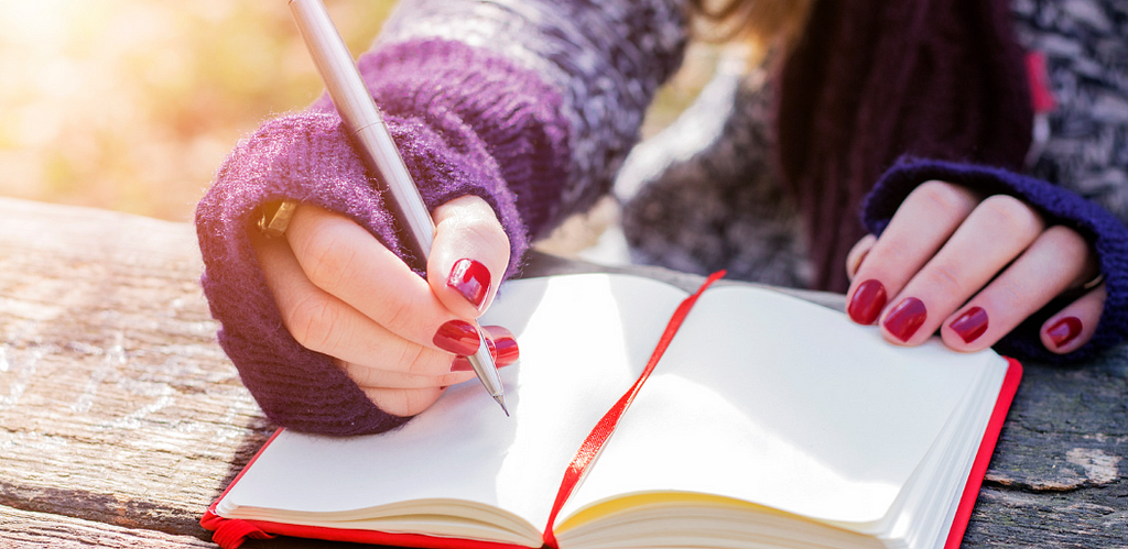 A close up image of an open journal with a hand holding a pen ready to write.