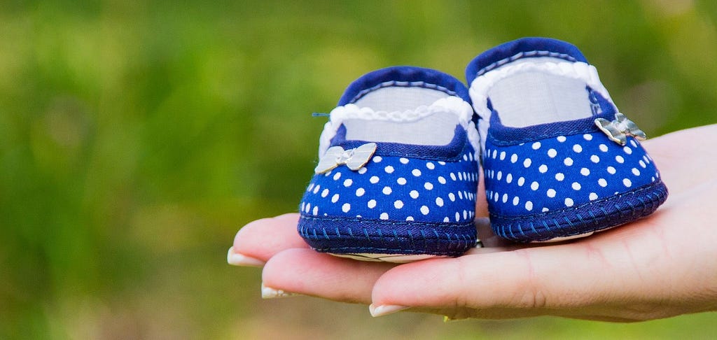 A pair of dark blue polka dot baby shoes balanced on the palm of a woman,