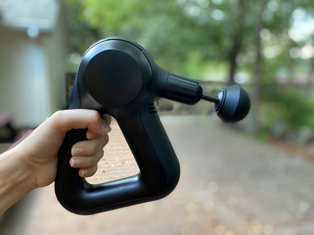 A close-up of a person holding a massage gun outside.