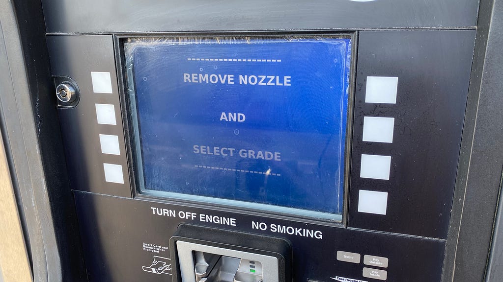 The blue payment screen at a gas pump that instructs you to remove the nozzle and select a grade.