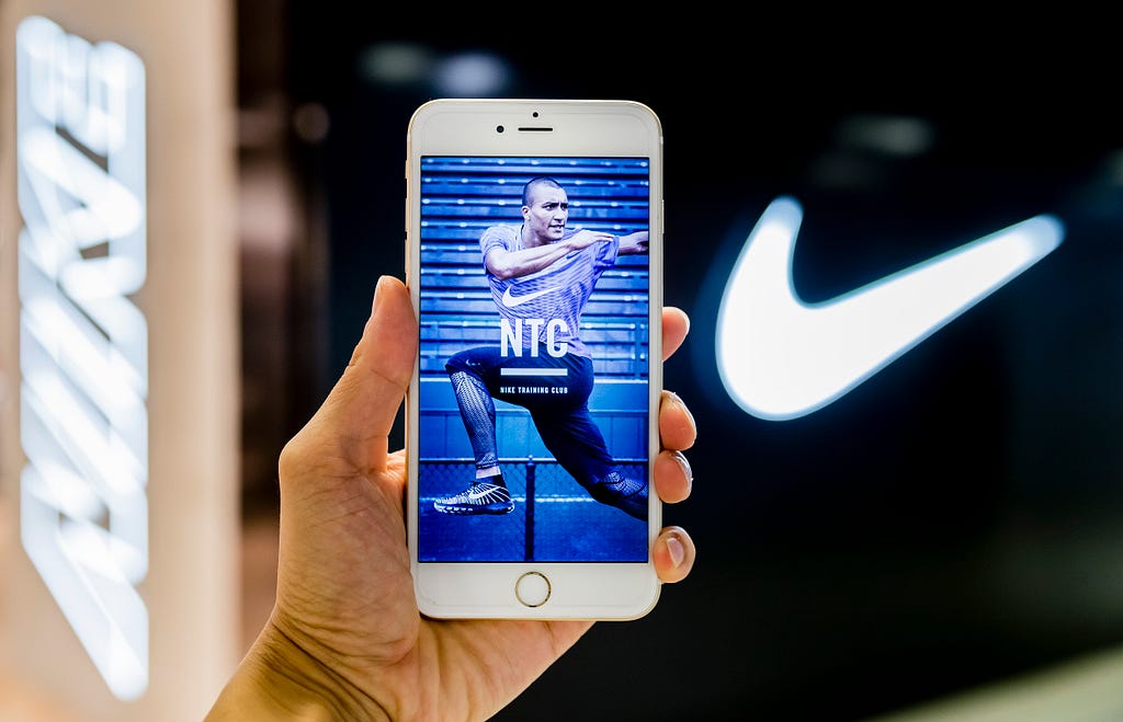 The Nike Training Club (NTC) app screen is displayed on a phone, held up against the Nike swoosh logo.