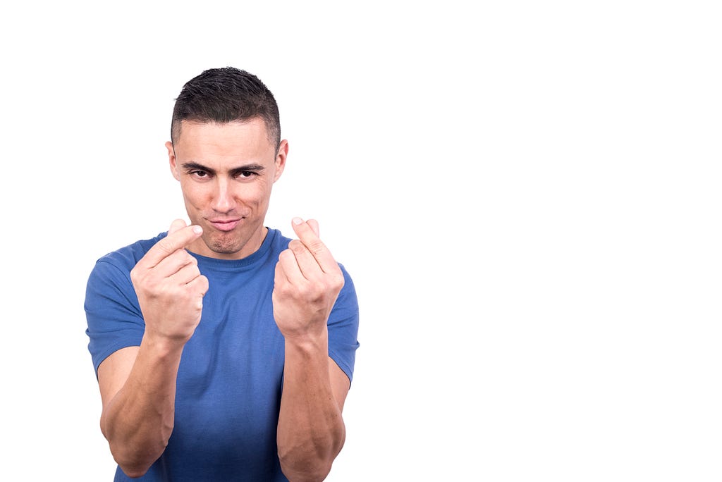 Image of a man wearing a blue t-shirt, making a confident and playful expression. He is gesturing with both hands, using his fingers to create a ‘money’ or ‘pay me’ sign.