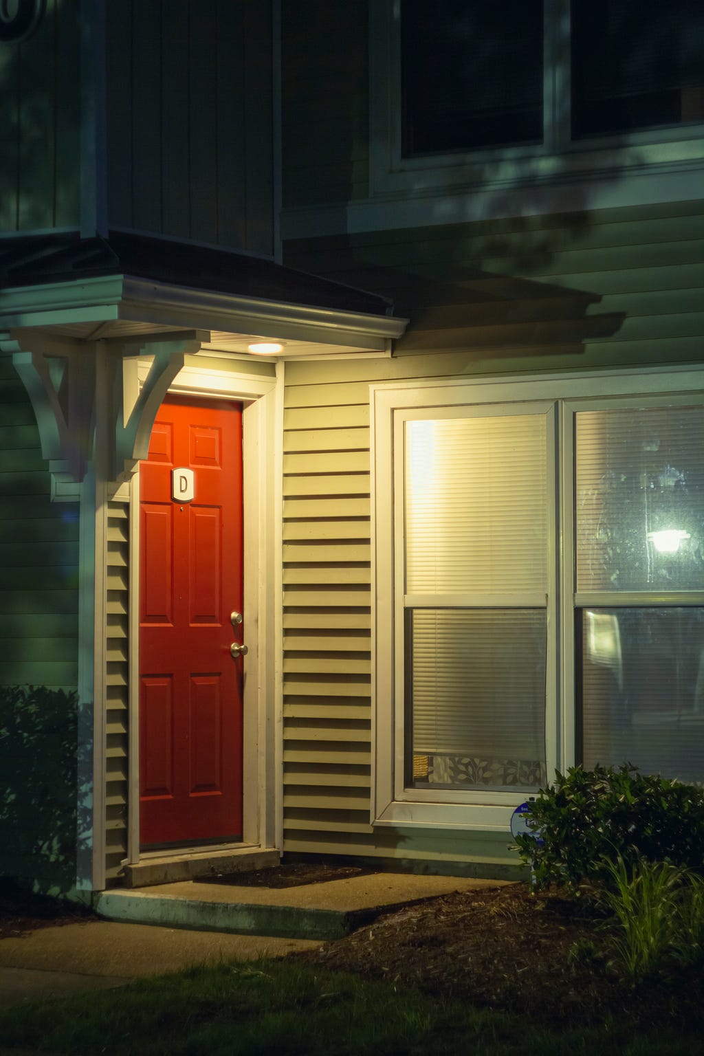 A red front door of an apartment, illuminated by a porch light