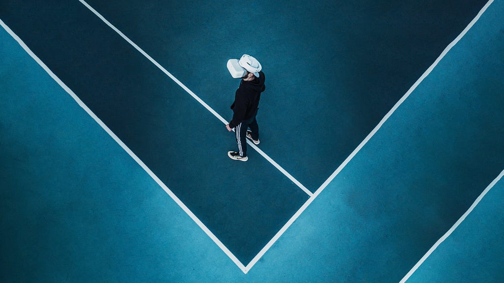 A man immersed in virtual reality is wearing a VR headset and walking on a blue tennis court. He seems to be lost in another universe