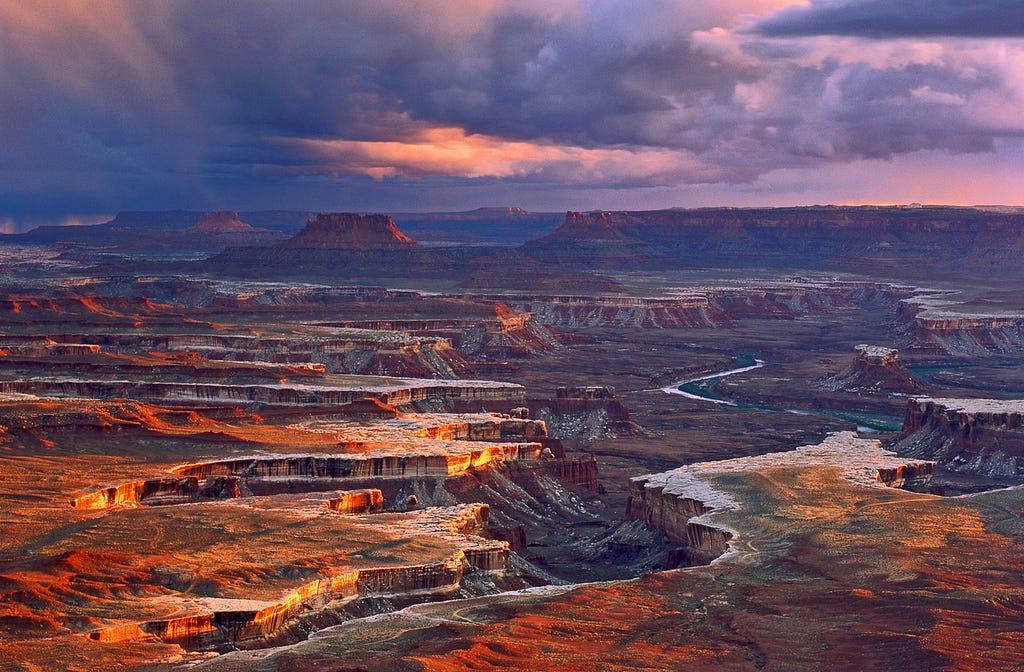 The Maze landmark in Canyonlands National Park. The image is of vast canyons that were once formed by rivers and water. It is beautiful, warm, full of colors, with a pink sunset.