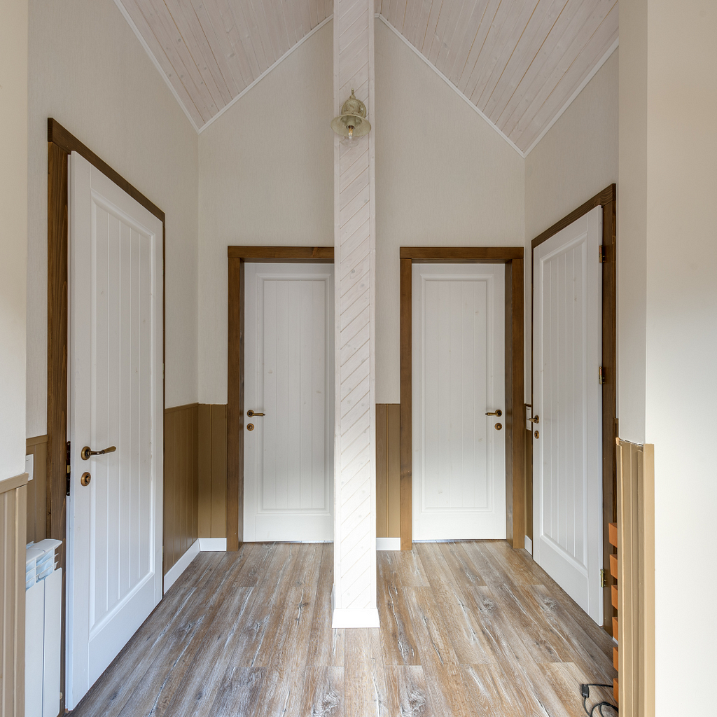 Within a two-toned hallway of white and brown, are four white doors. Two are across from each other. Two are directly next to each other.