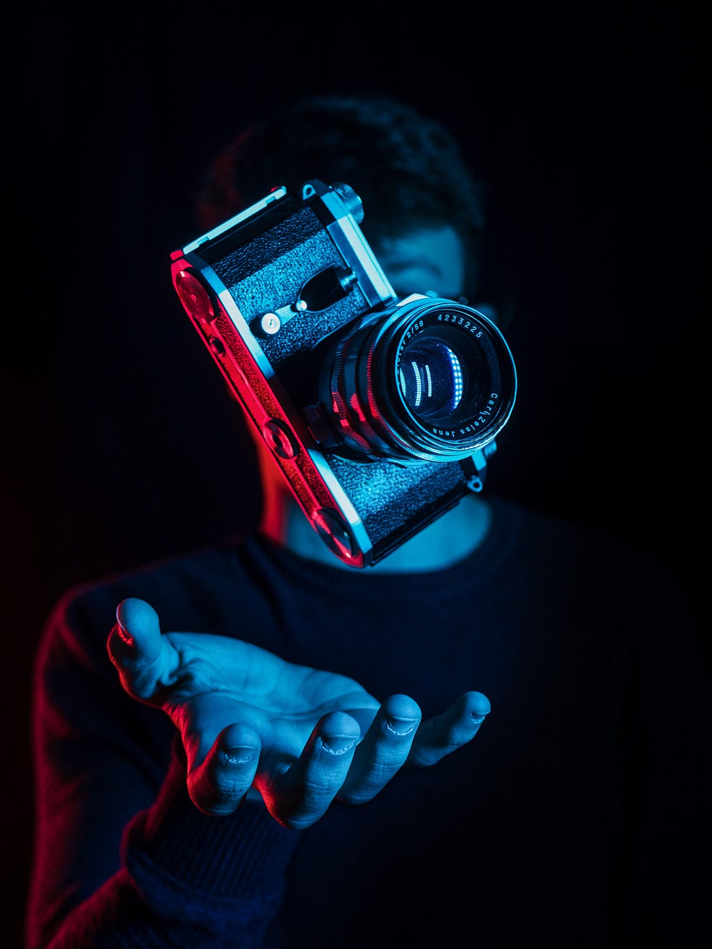 A classic camera is tossed in the air with a blue and red treatment in a low-key setting.