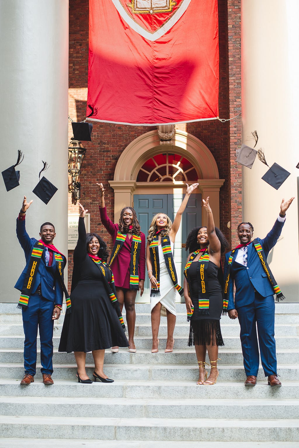 A group of six recent graduate students throw their graduation caps into the air in a celebratory mood.