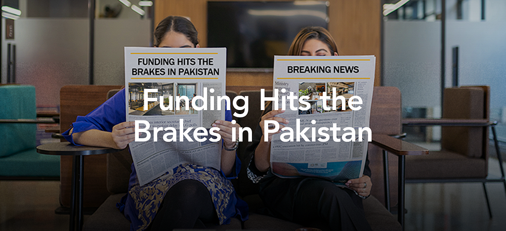 Two women holding up newspapers which read “Funding Hits the Brakes in Pakistan”.