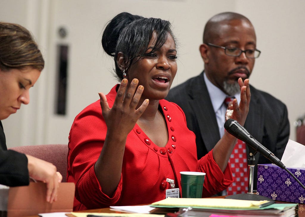 A photo of Kelley Williams-Bolar speaking into a microphone. She sits between two people.