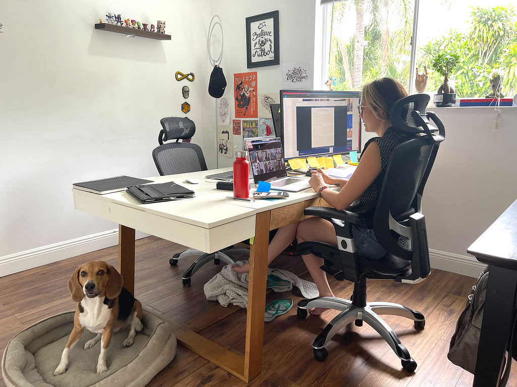 Karo sitting in workshop at computer with her dog at her feet.