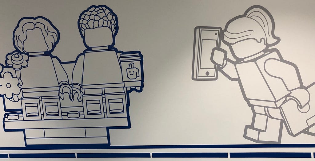 Outline of two LEGO Minifigures on a couch, one holdings flowers and the other holding a cup. Another LEGO Minifigure walking towards them holding a phone and a folder.