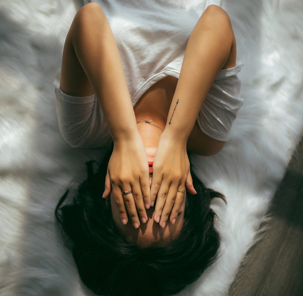 Girl lying on a white background covers her face with her hands