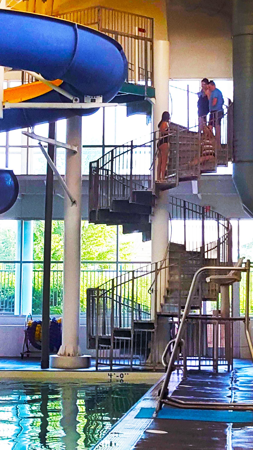 Spiral staircase one story tall leading to a waterslide. Girl is sitting on steps pulling herself up them. 3 friends nearby.