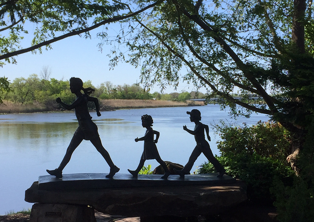 Statues of three young people walking, set next to a river.