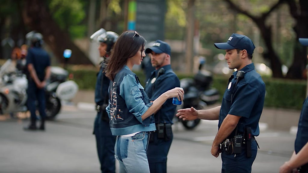 Kendall Jenner handing a policeman a can of pepsi