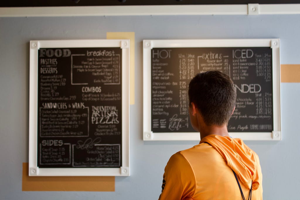 Photo from behind of a man looking at a cafe menu board