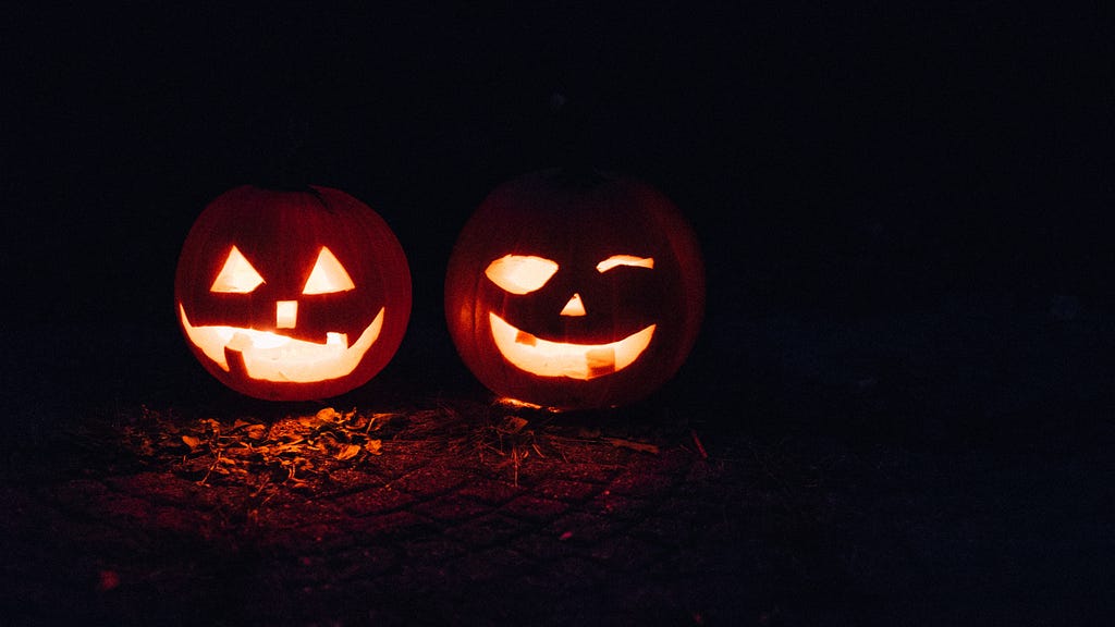 An image of two jack-o-lanterns (pumpkins with faces carved into them) in the dark lit up.