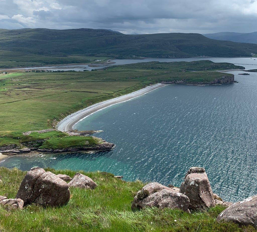 Peninsulas of scottish coastline stretch out into the sea loch of shallow blue water.