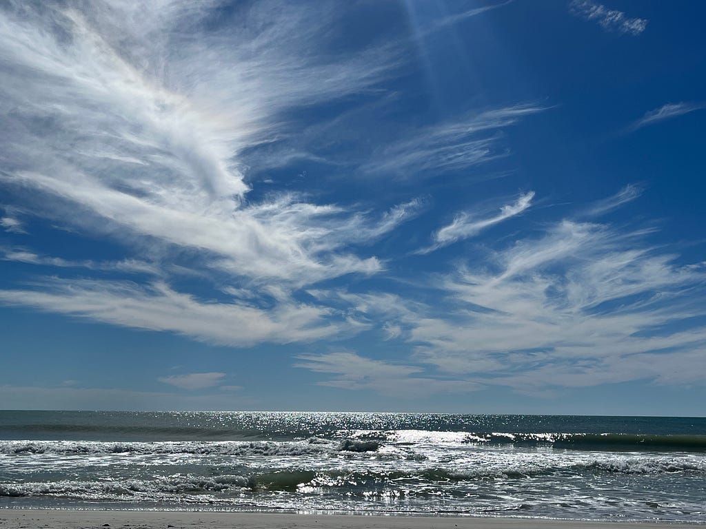 Florida Gulf beach view. Sunlight sparkling on water with wispy clouds.