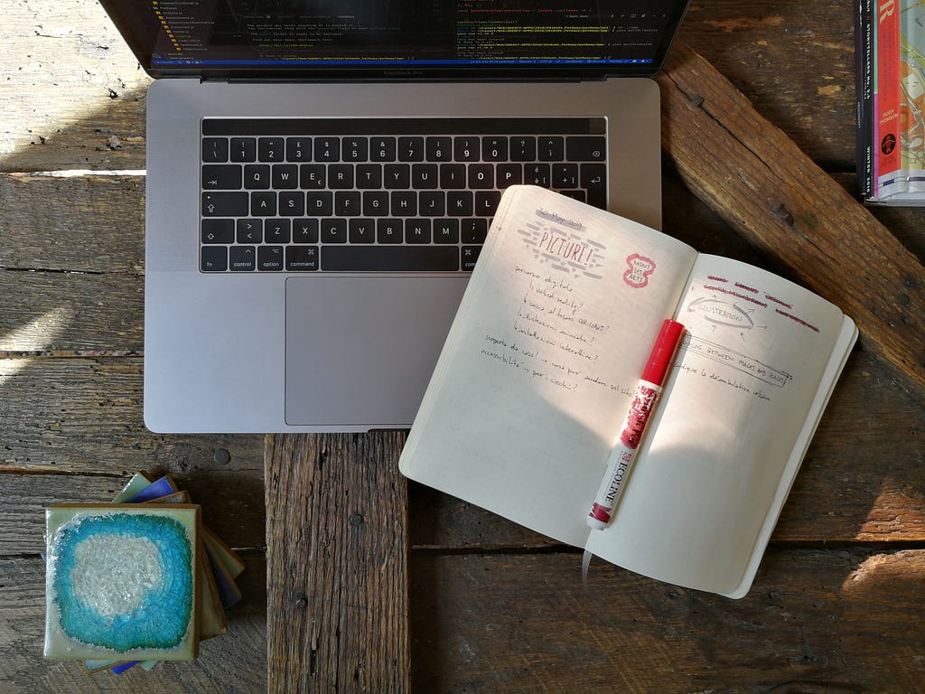 A laptop displaying code and a notepad, on a rough wooden table top