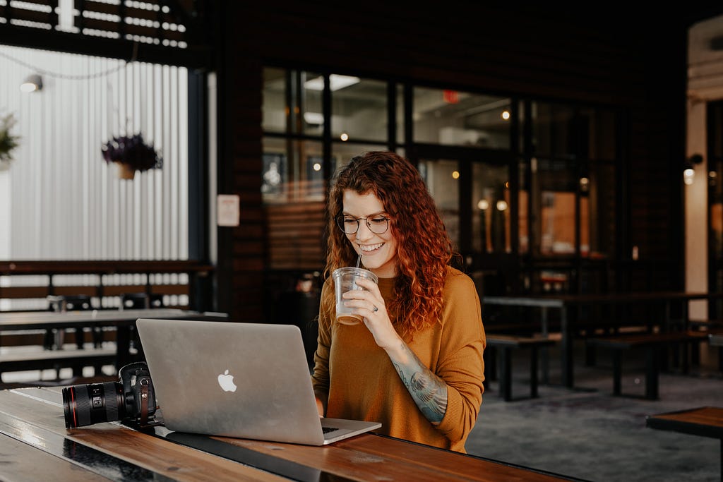 Woman with red hair sipping an iced coffee while using a computer