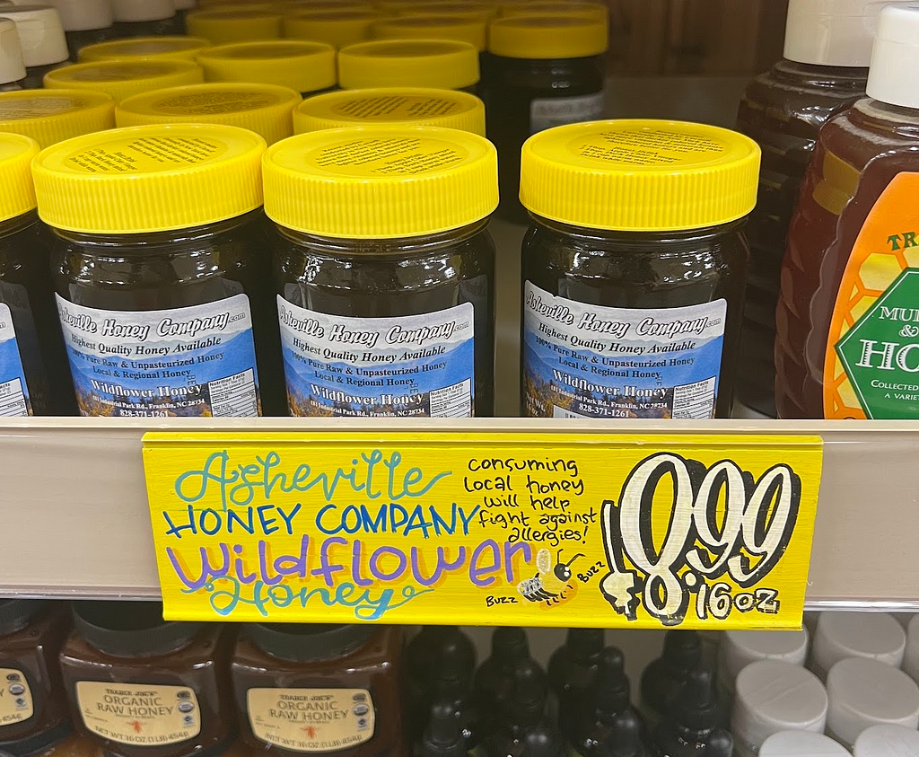 Product tag that says “Asheville Honey Company Wildflower Honey (consuming local honey will help fight against allergies)”