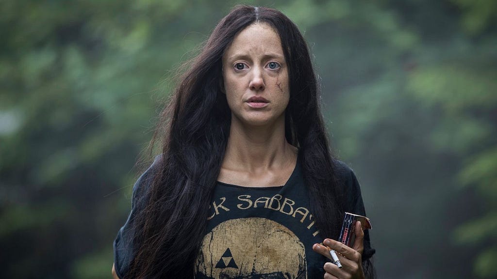 Mandy (Andrea Riseborough) is wearing a Black Sabbath T-shirt and staring into the distance. She is carrying a book and holds a cigarette between her fingers.