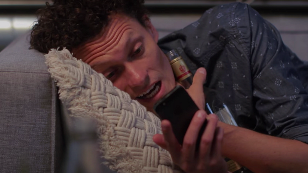 A photo of a seemingly drunk guy holding his phone and a bottle of beer