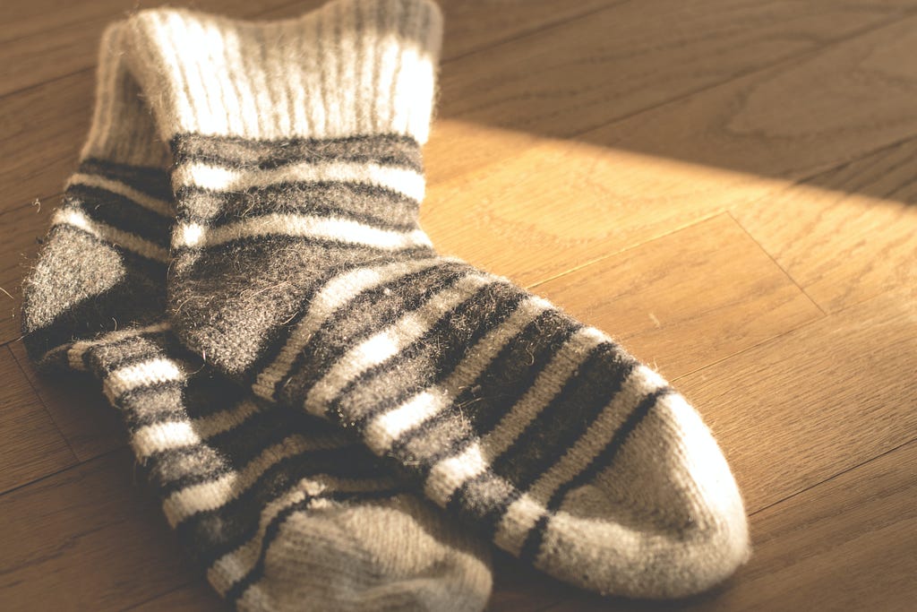 Cozy woollen socks placed in the sunlight on wooden floorboards