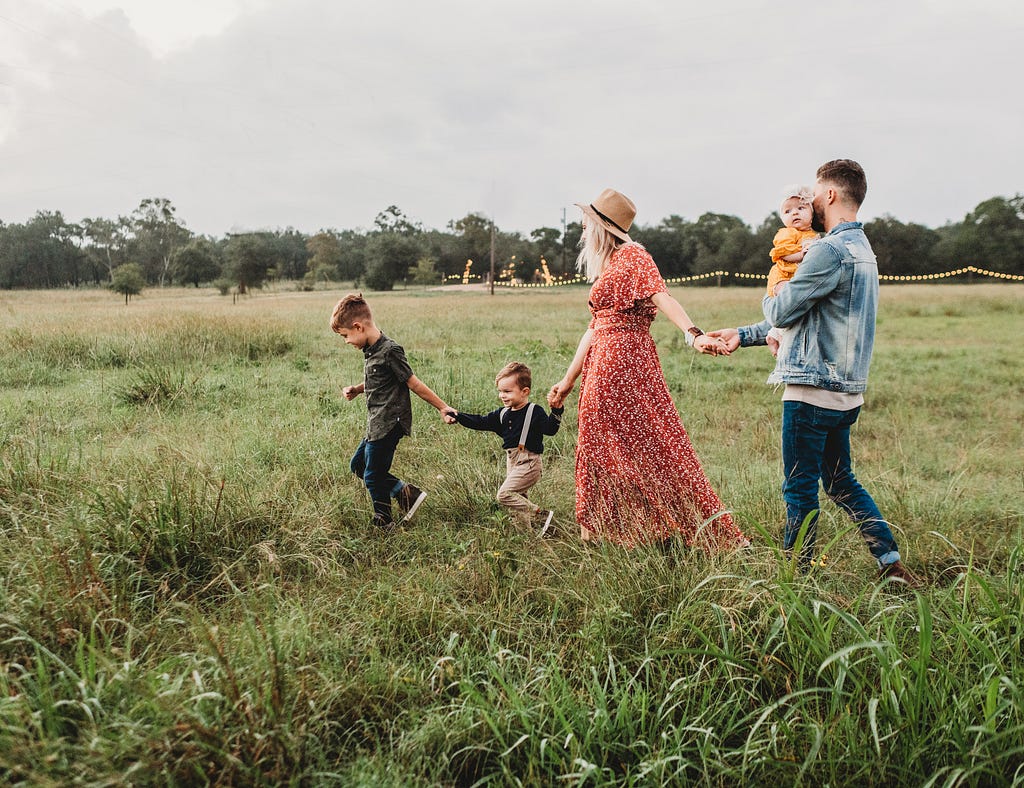 Mother and father hold hands with their children as they walk through a field.